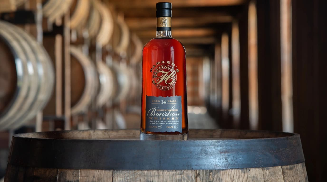 Parker's Heritage Collection 20th Edition bottle, labeled Aged 14 Years and 118 proof, standing on a barrel head in a Heaven Hill rickhouse with rows of barrels receding behind it