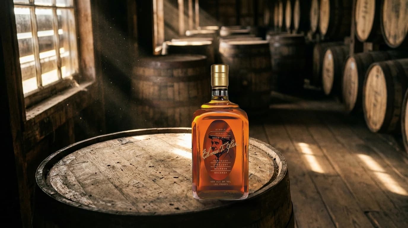 A bottle of Elmer T. Lee Single Barrel Kentucky Straight Bourbon standing on a barrel head inside a Kentucky rickhouse, rows of aging barrels behind it in low autumn light